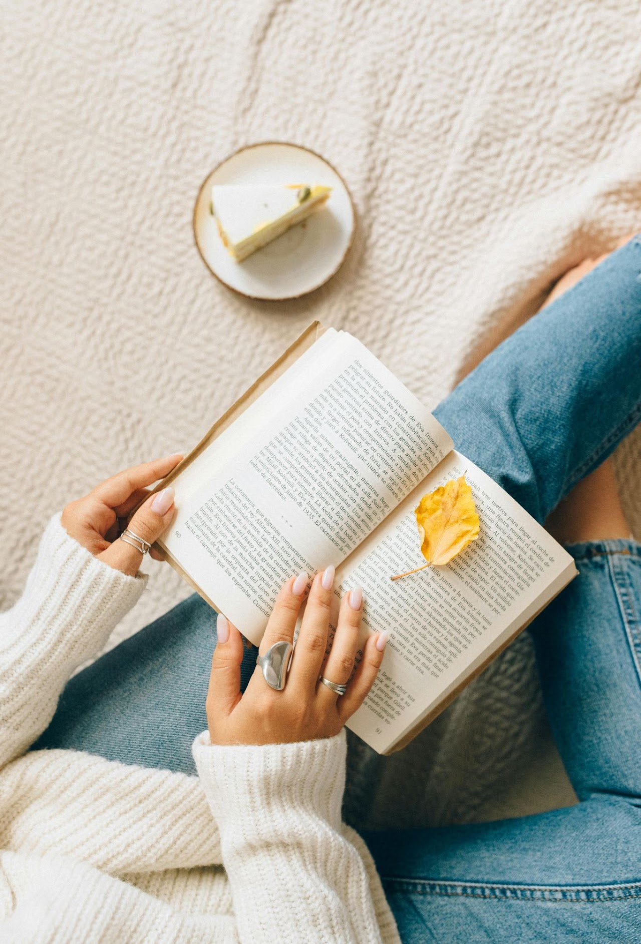 Person reading a book with cake nearby